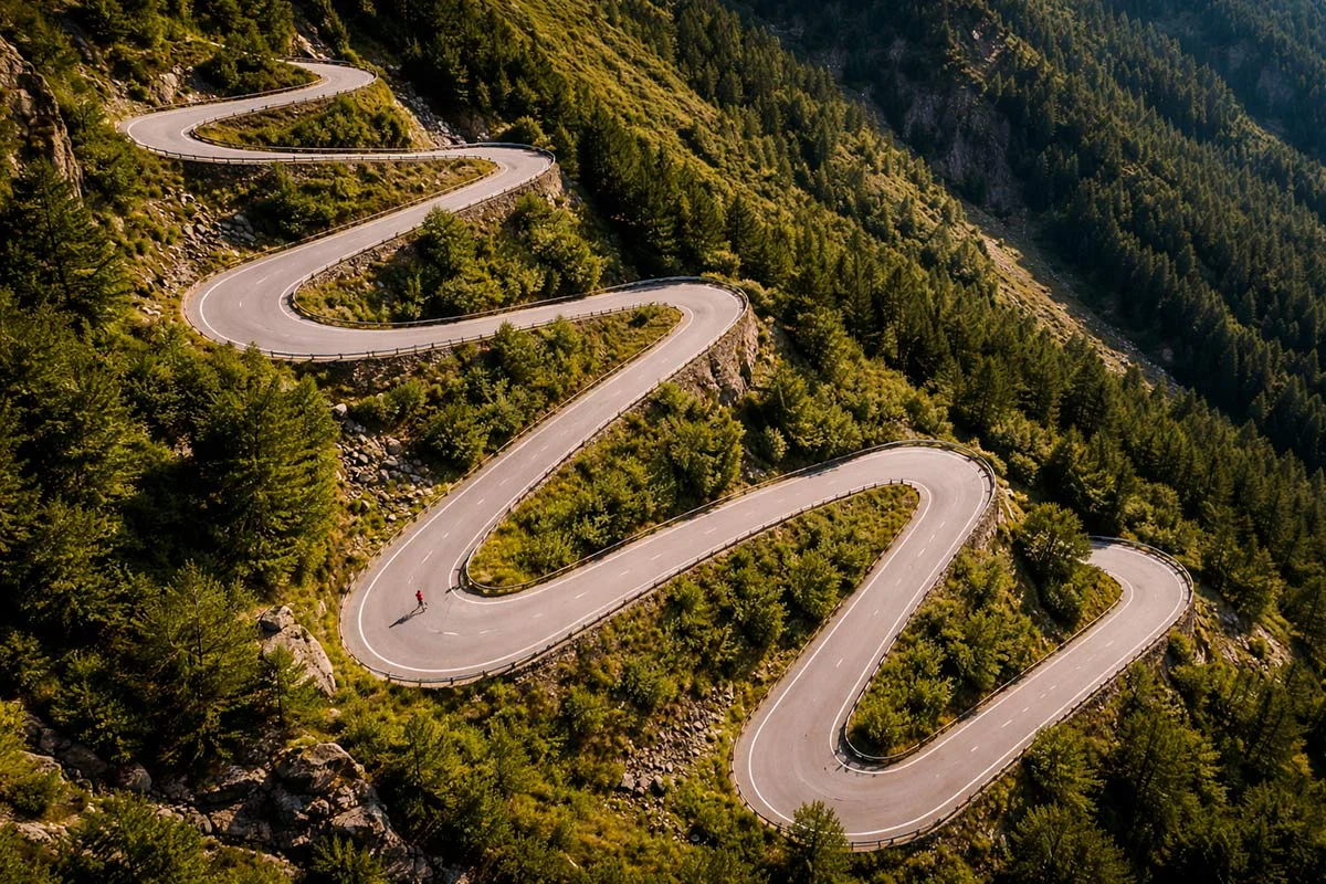 Strada di montagna con tornanti e un ciclista in salita visto dall'alto